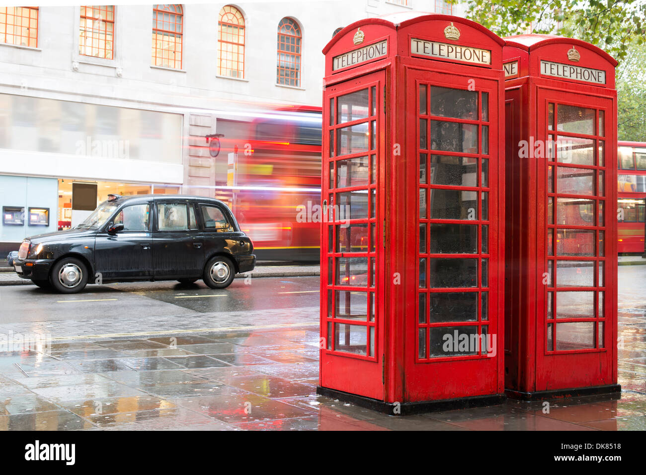 Red Phone cabines in London and vintage taxi.Rainy day. Vintage phone cabine monumental Stock Photo