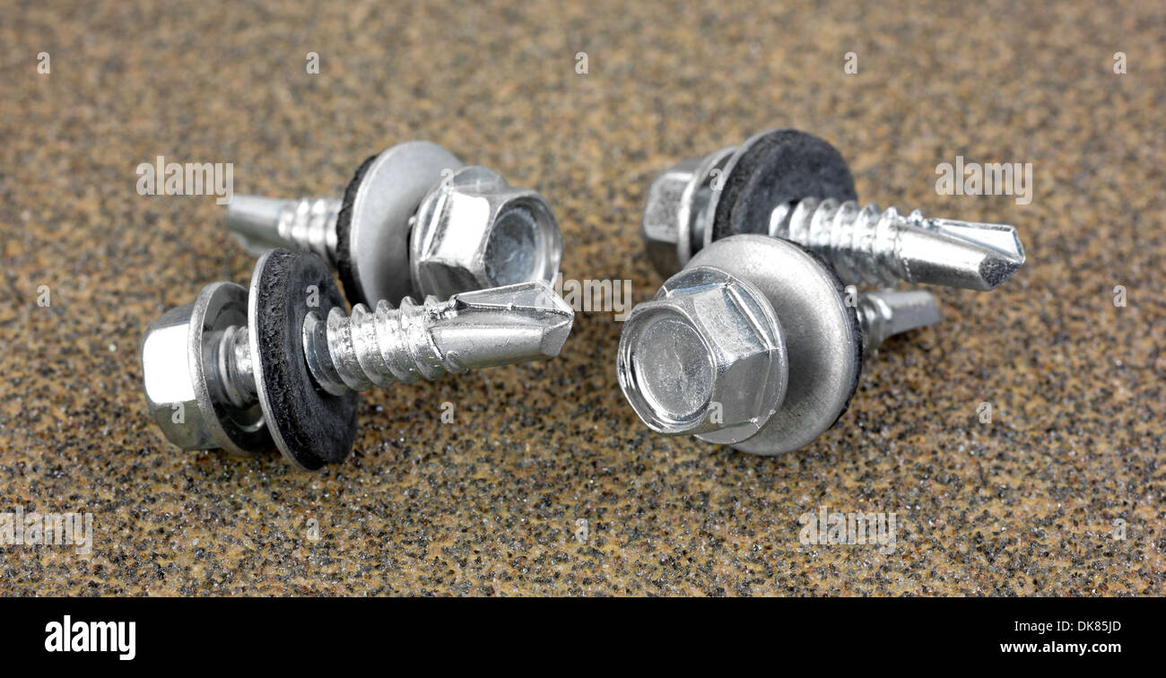 A group of four rubber bonded sheet metal screws on a piece of coarse sandpaper. Stock Photo