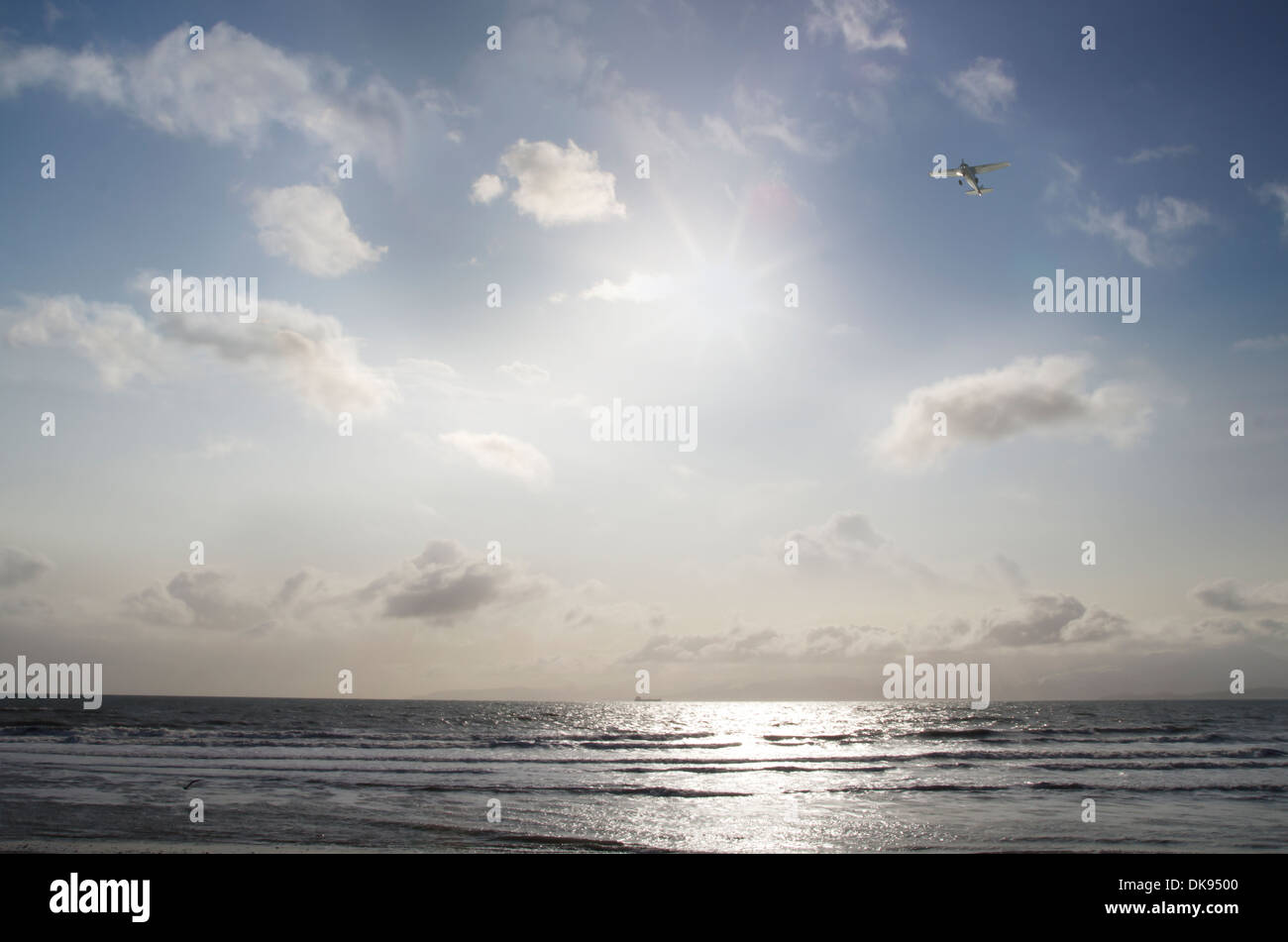 Small airplane flying over the ocean with a sunburst and clouds. Stock Photo
