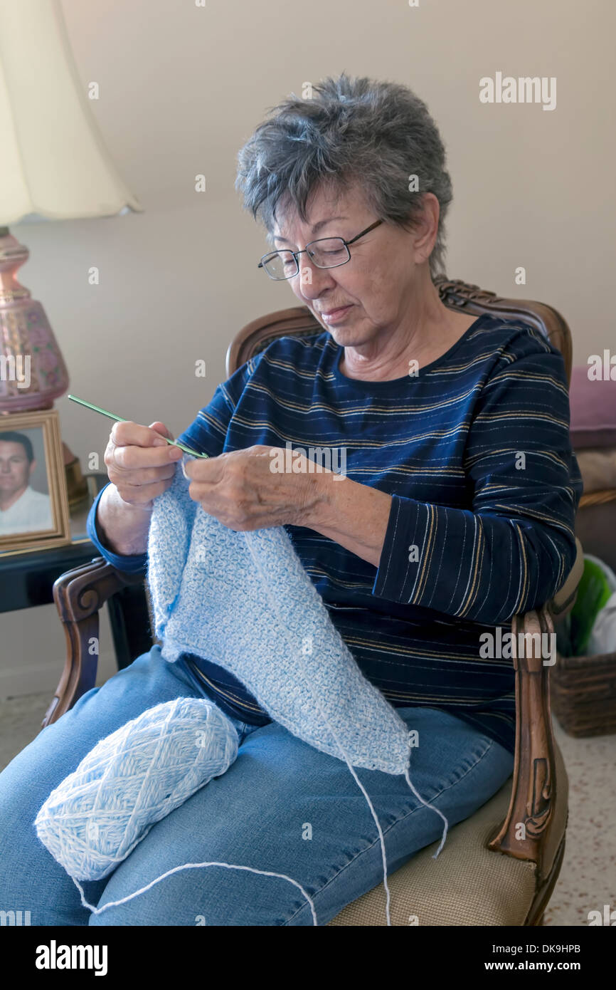 Closeup of the hands of a mature older woman, part native American, crocheting a pale blue wool baby's blanket, USA. Stock Photo
