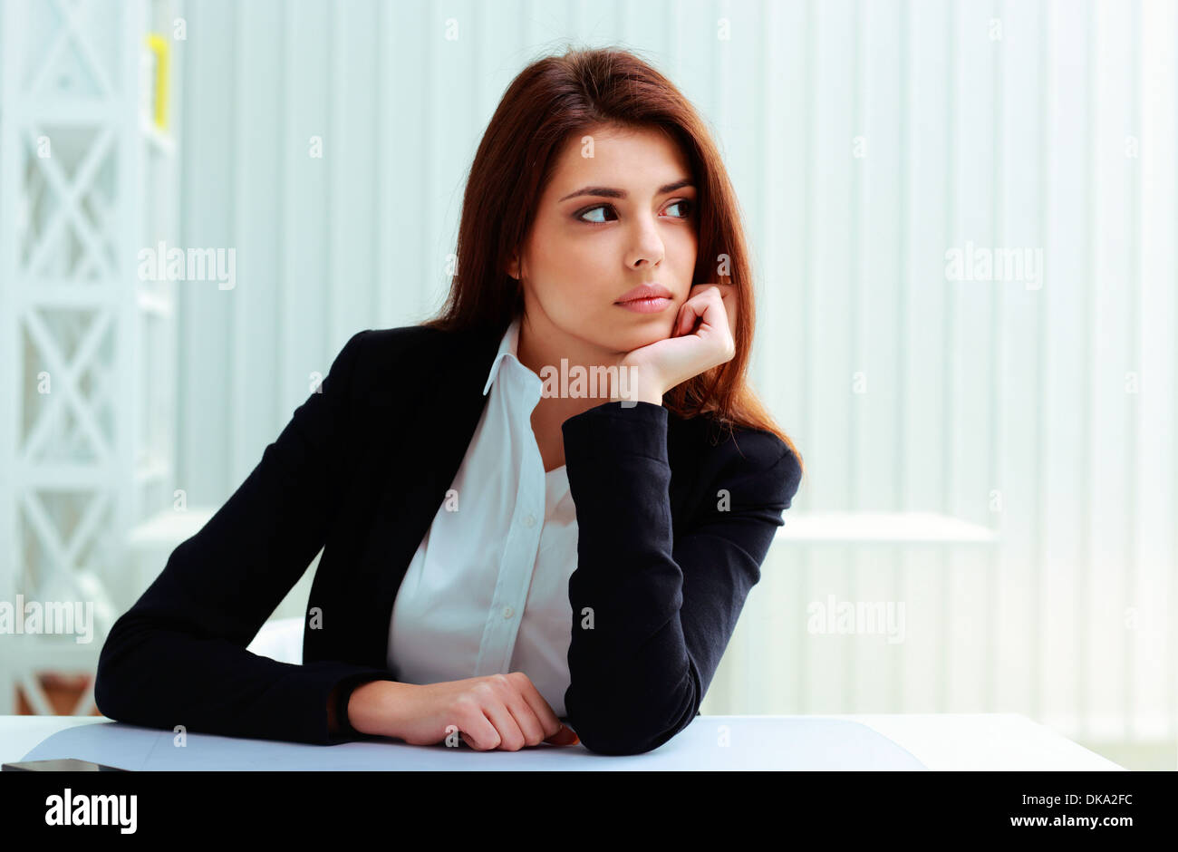 Young thoughtful businesswoman sitting on her workplace and looking away in office Stock Photo