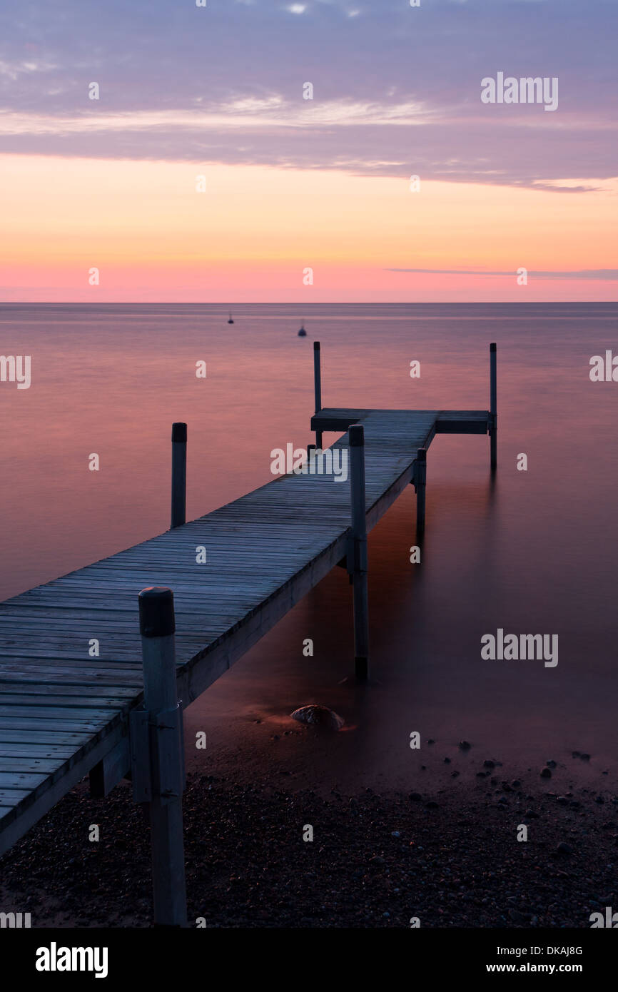 Long wooden bridge leading from ground into the sea at sunset at calm weather. Stock Photo