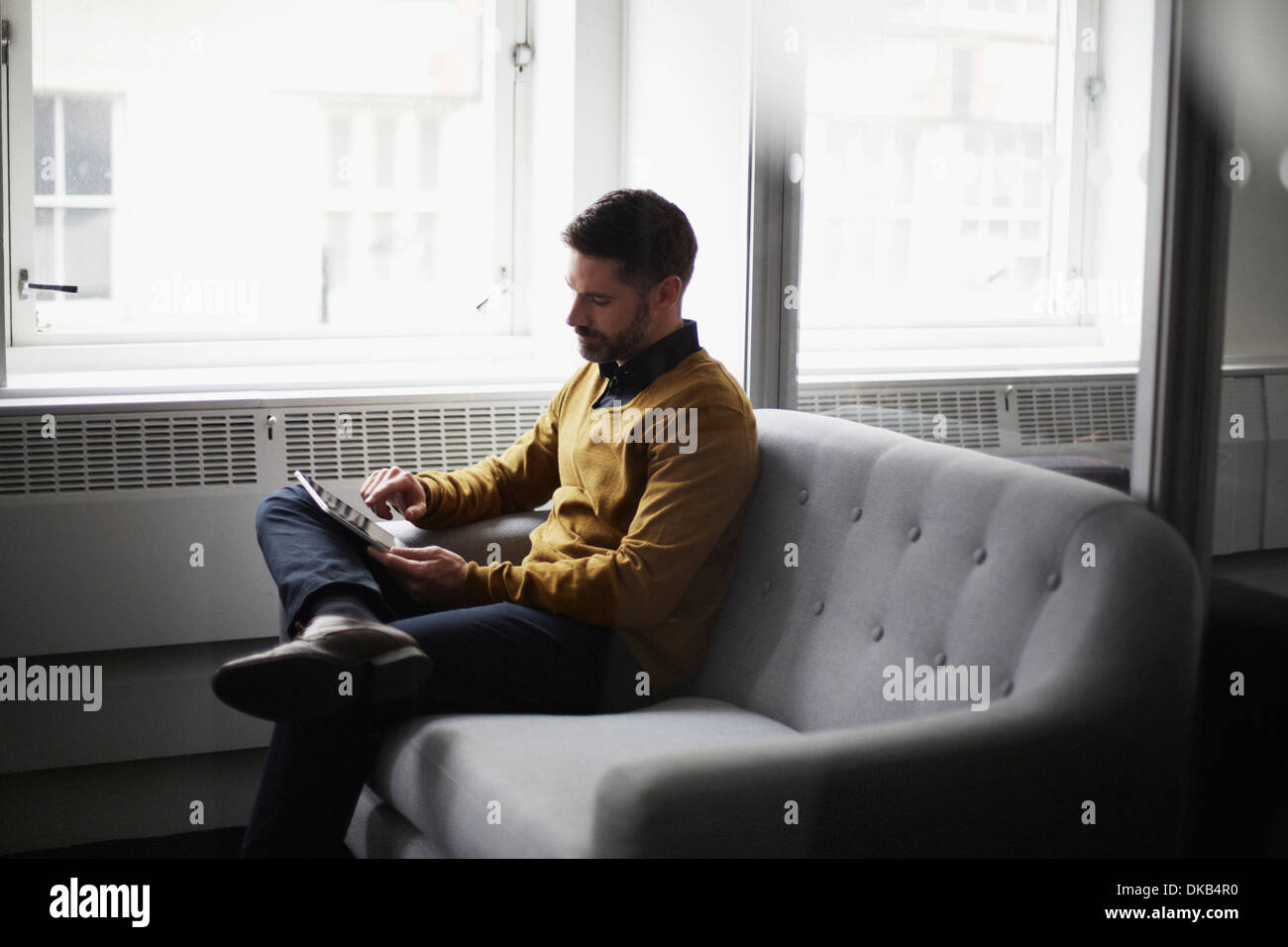 Casual businessman sitting on sofa using digital tablet Stock Photo