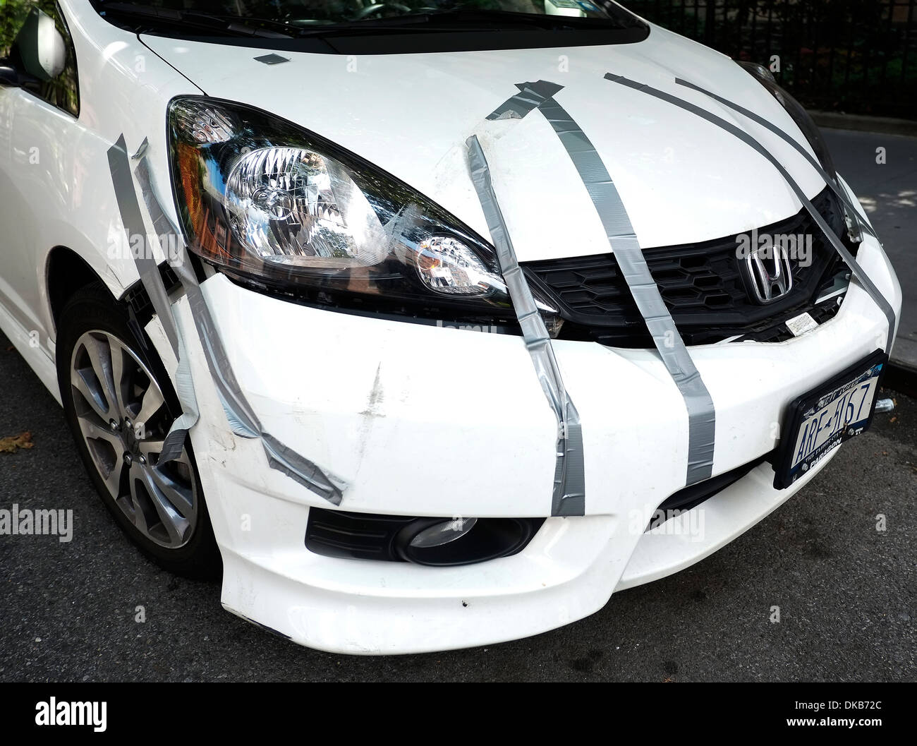 The front end of a white parked car held together with silver duct tape. Stock Photo