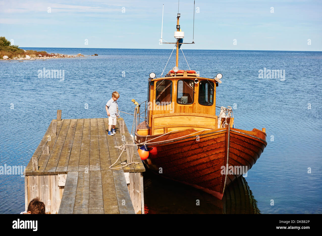 Boy on pier by boat, Eggergrund, Sweden Stock Photo