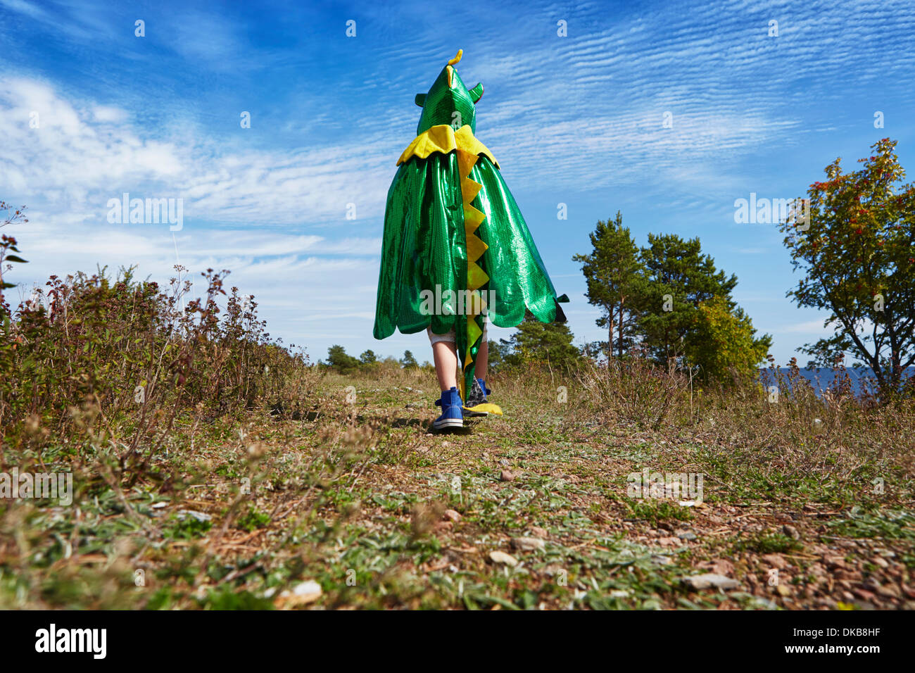 Boy wearing green cape walking along grass, Eggergrund, Sweden Stock Photo
