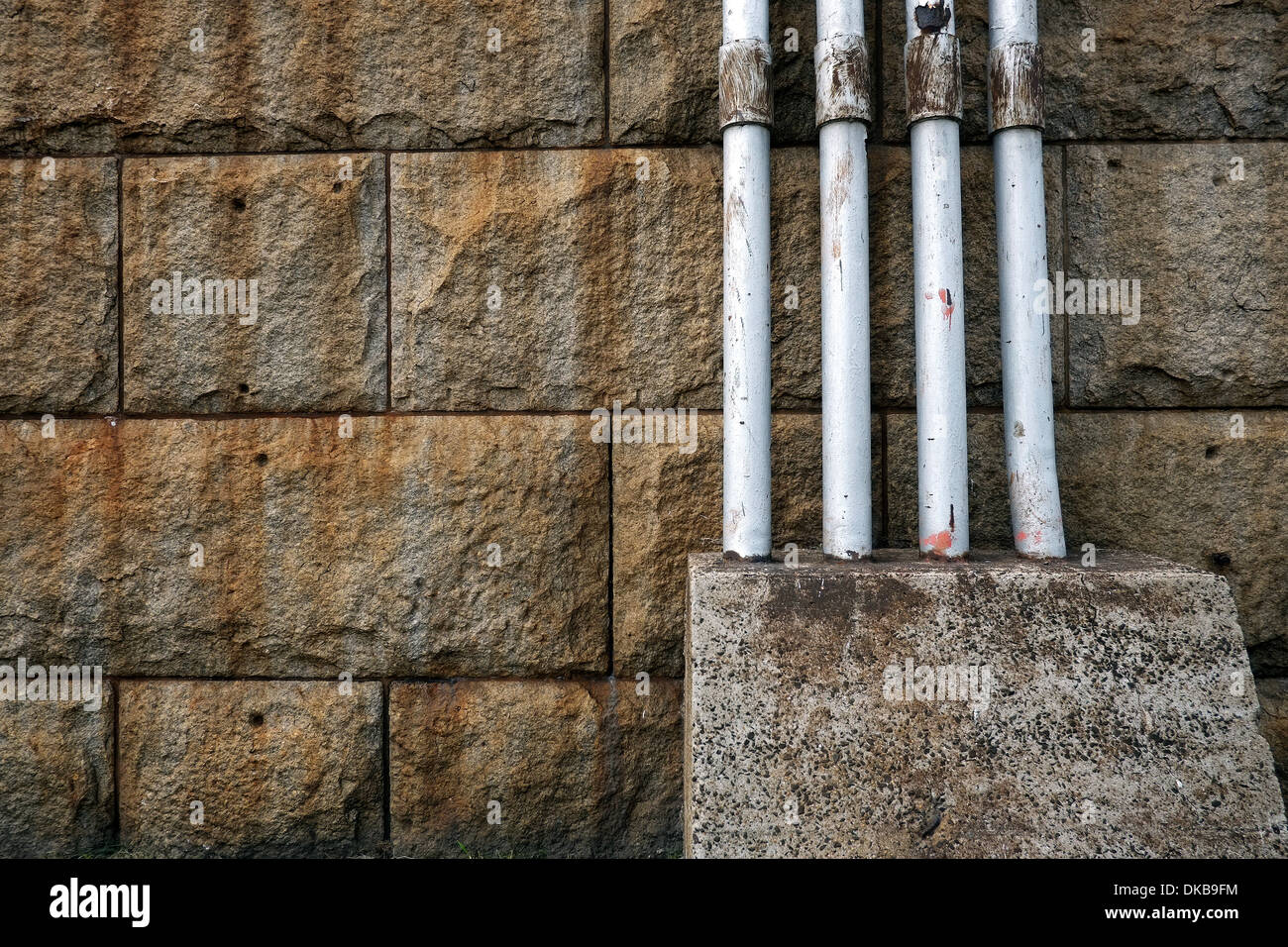 Pipes embedded in a concrete block against a stone wall. Stock Photo