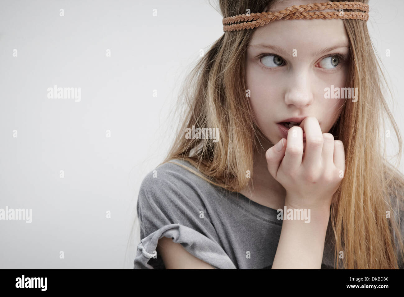 Portrait of girl wearing leather braid around head, holding feather, finger in mouth Stock Photo