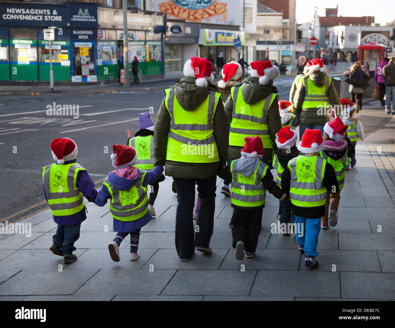 K ids walking across street in Blackpool, Lancashire, UK 4th December, 2013.   Rear view of risk assessed Pre-school children and teachers, safeguarded wearing santa hats & high visibility clothing, en-route to the Winter Gardens Blackpool Opera House Theatre Open day.  An opportunity to access all areas, free of charge, something never done before at the Winter Gardens, to celebrate 135 with the local community and visitors of Blackpool. Stock Photo