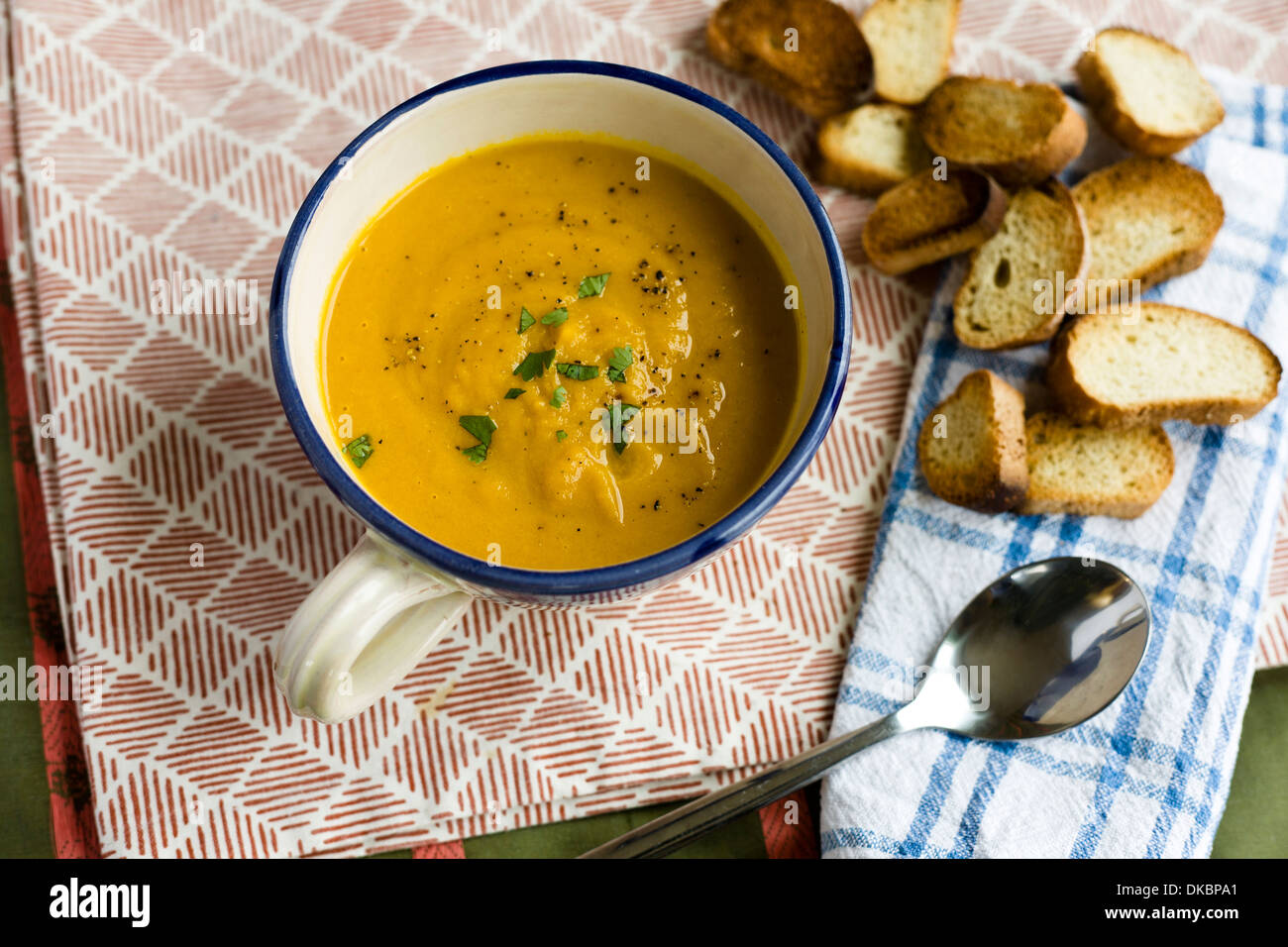 Top down view of a large mug of carrot and coriander soup, with spoon and croûton. Stock Photo
