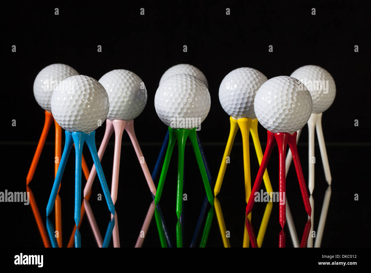 White golf balls and different colored tees on a black desk Stock Photo