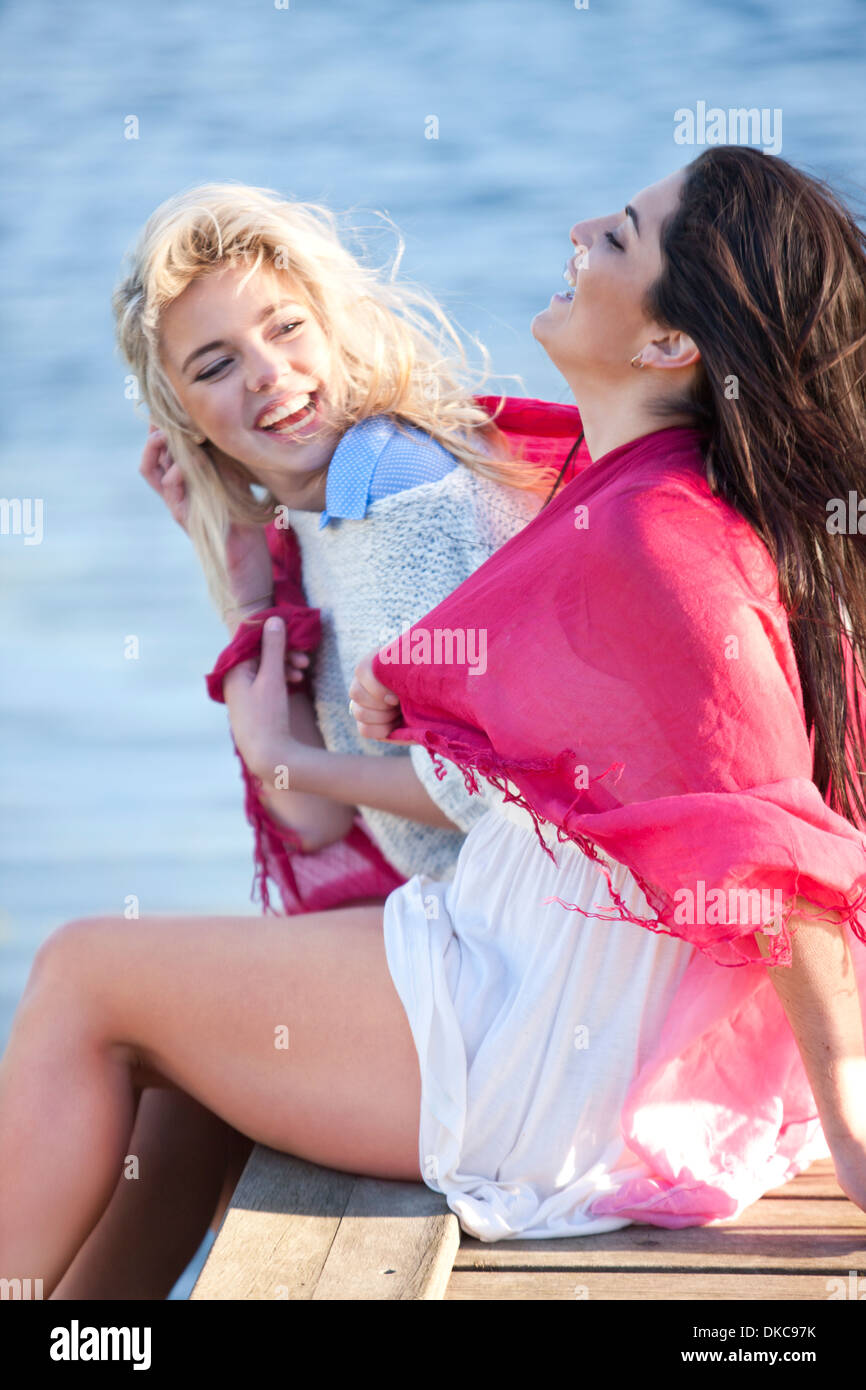 Two female friends sitting on pier laughing Stock Photo