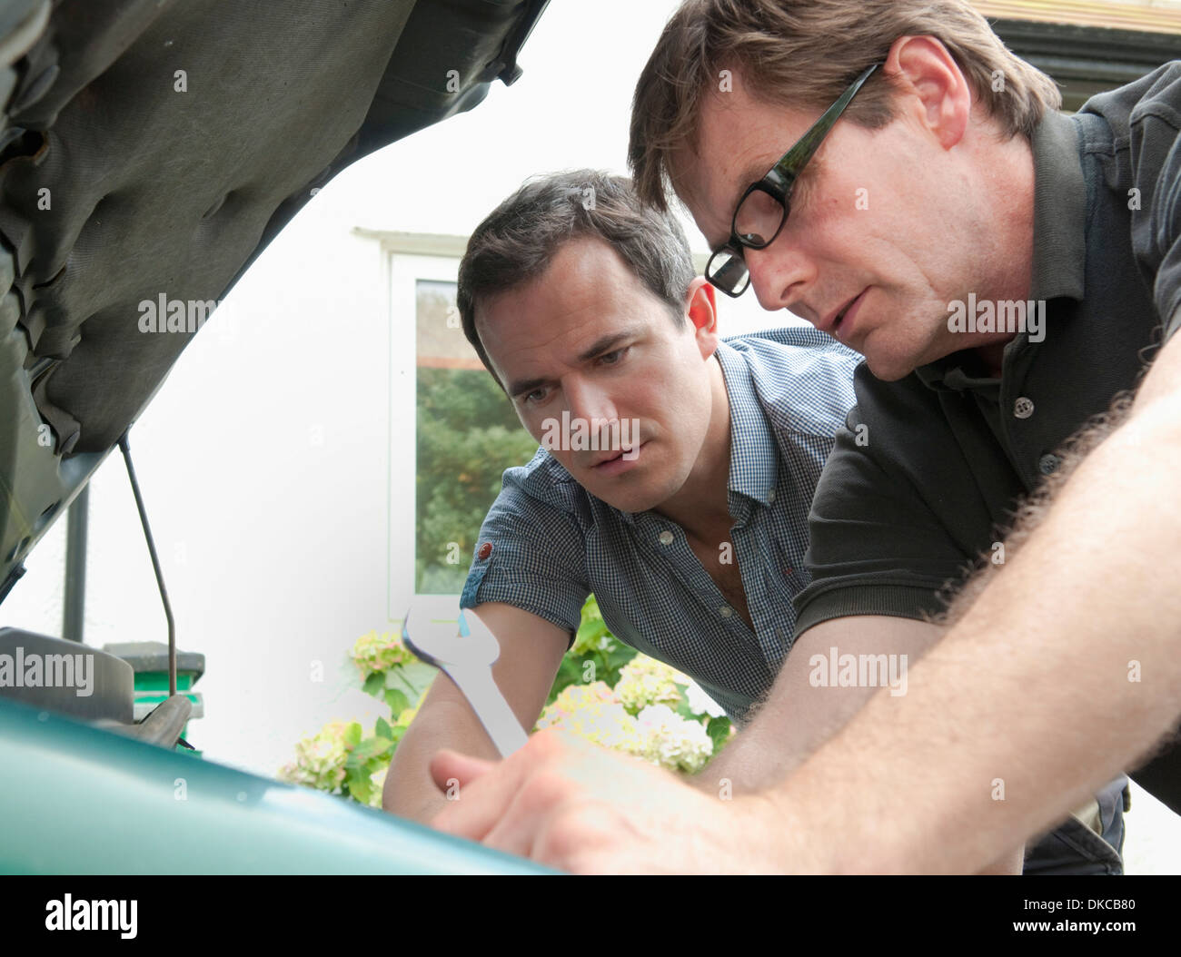 Two male adult friends checking under car hood Stock Photo