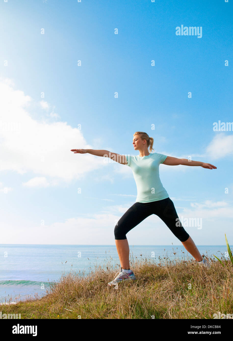 Mid adult woman stretching on cliff top, Thurlestone, Devon, UK Stock Photo