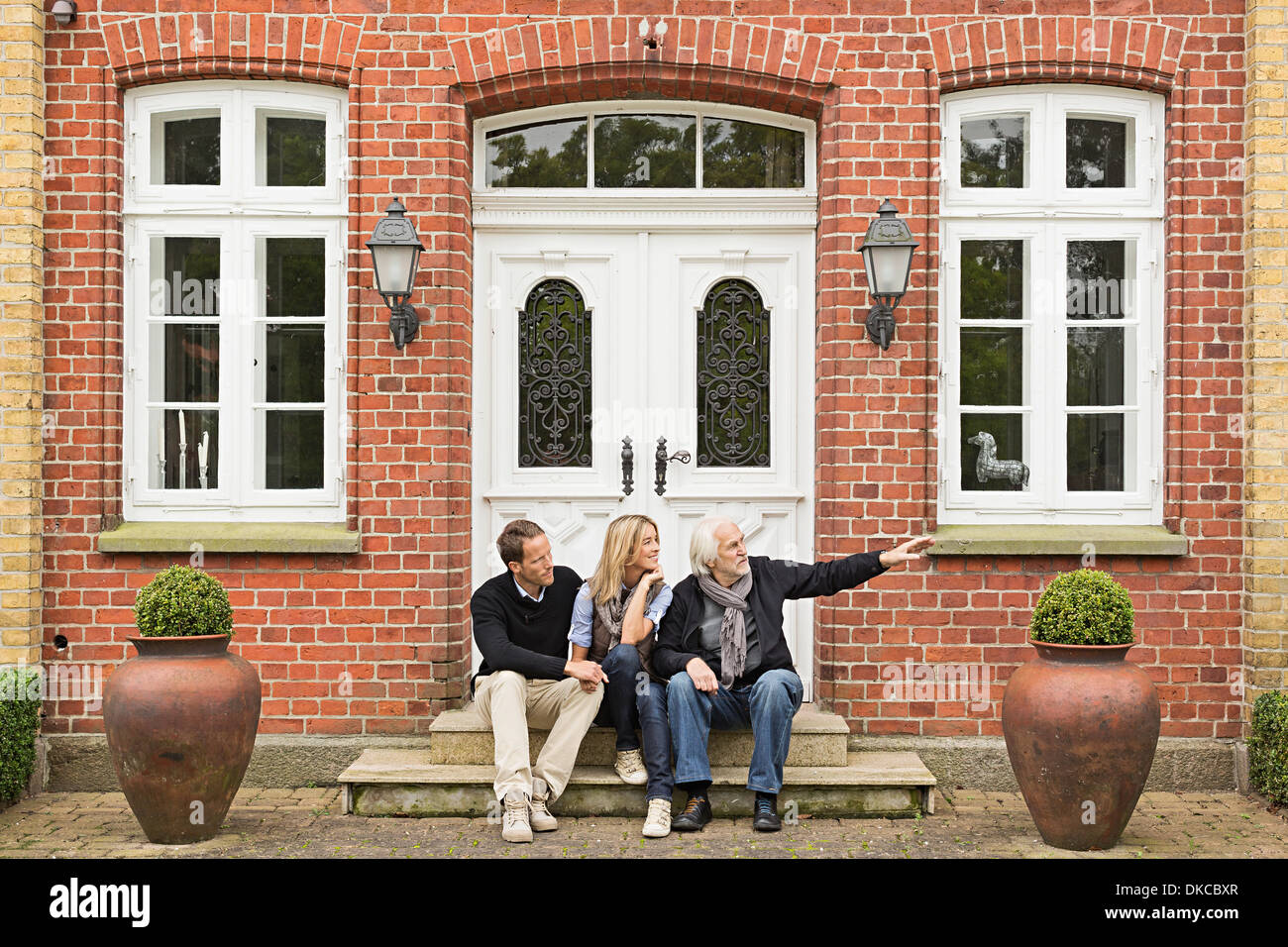 Father and mid adult couple sitting on doorstep Stock Photo