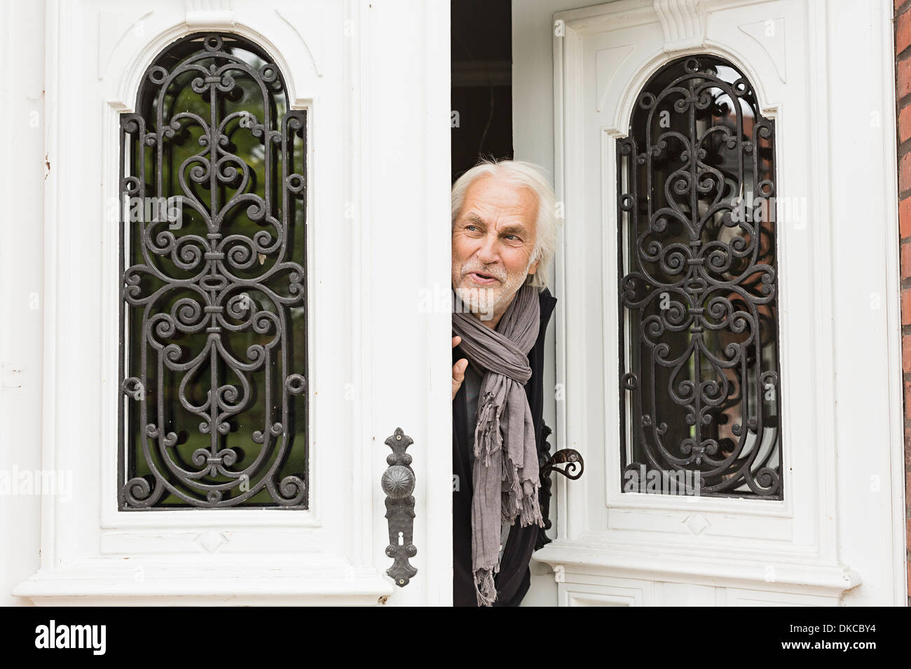 Senior man peeking through doorway Stock Photo