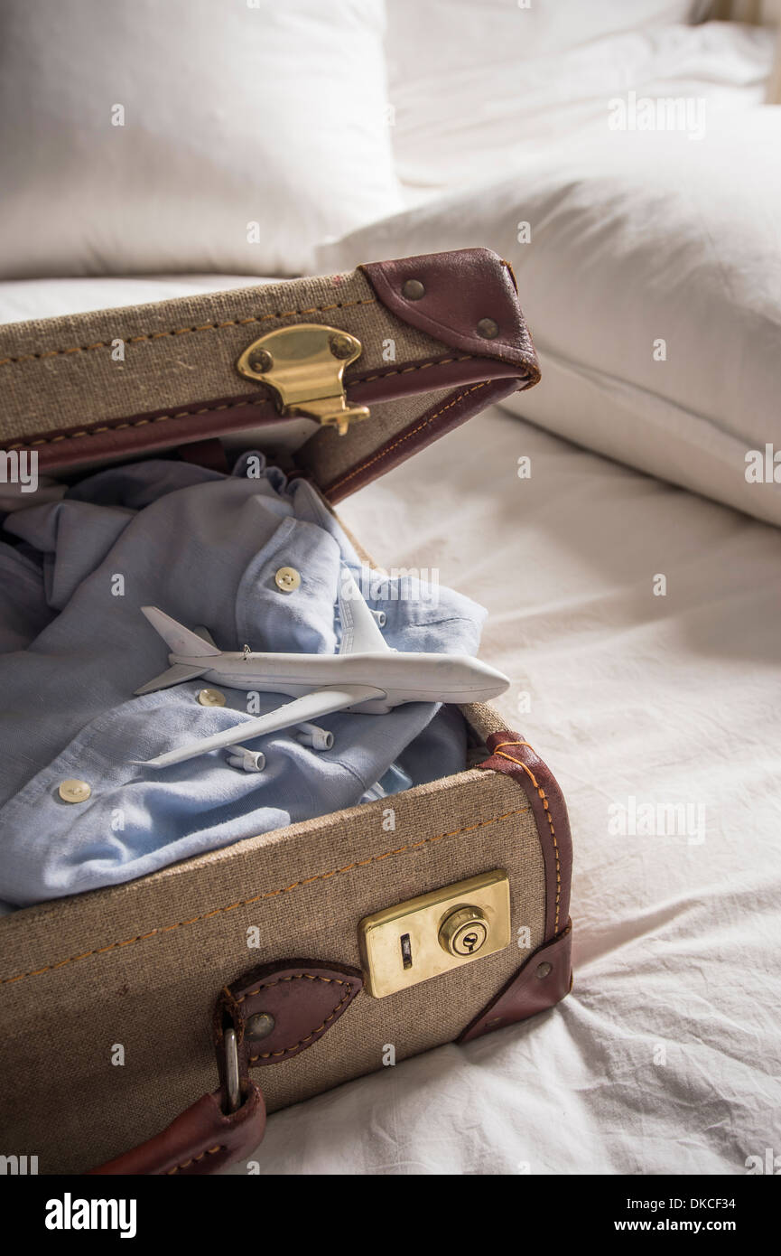 Open suitcase on bed with shirt and toy airplane Stock Photo