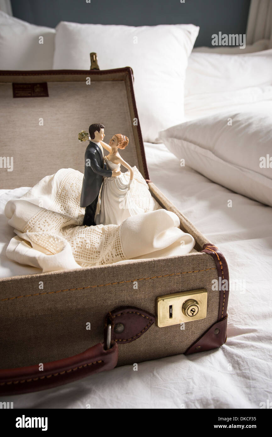 Open suitcase on bed with wedding figurines Stock Photo