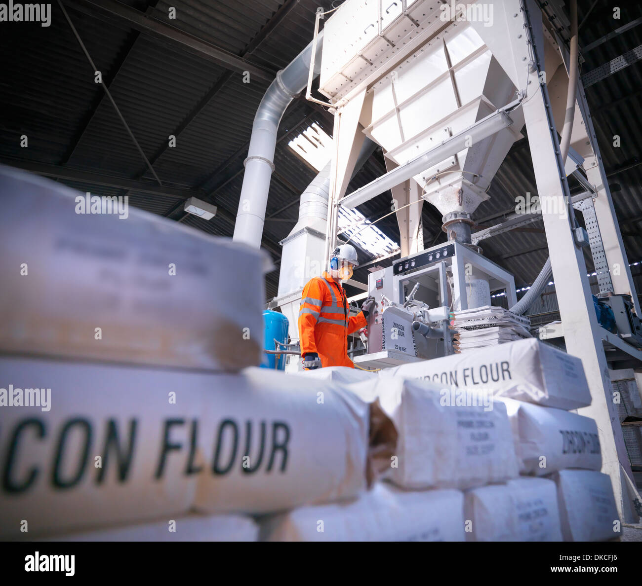 Worker in protective clothing filling zircon flour bags in mill, low angle view Stock Photo