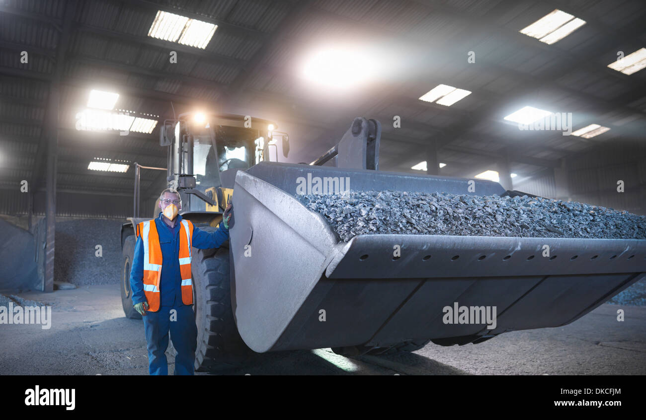 Worker in mineral store next to digger full of metal alloy Stock Photo