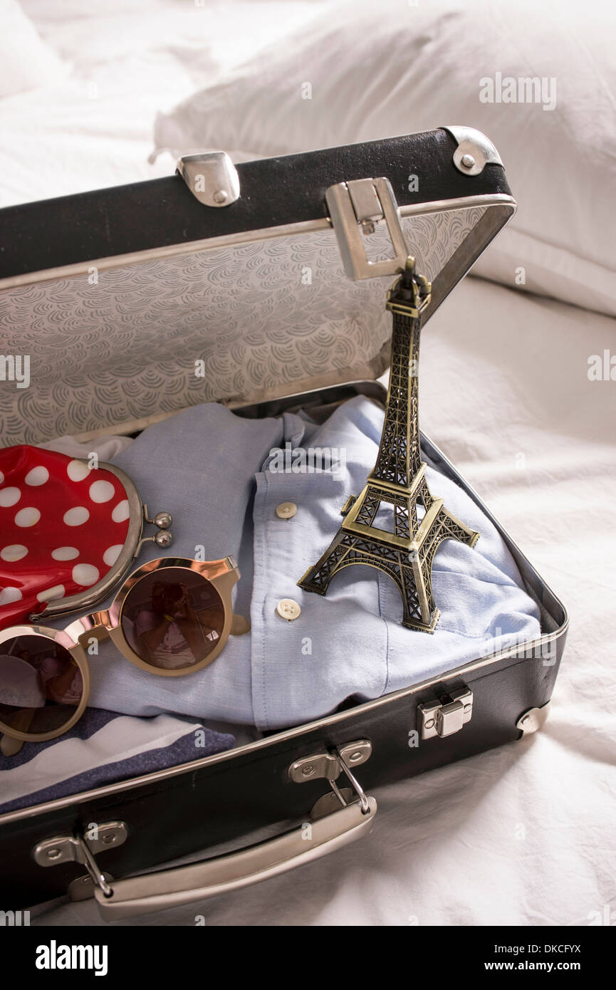 Open suitcase on bed with eiffel tower souvenir and sunglasses Stock Photo