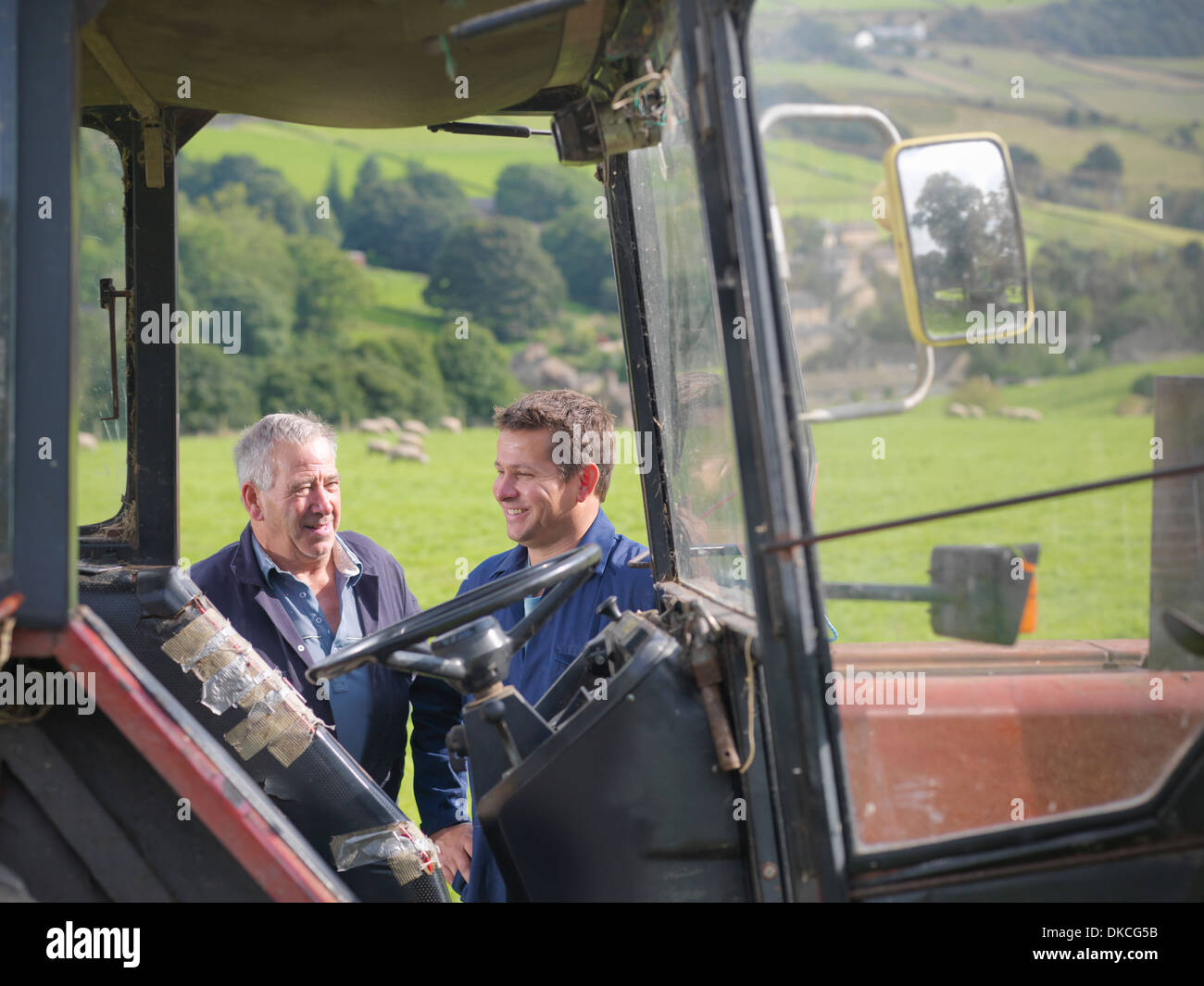 Farmer and son talking next to tractor in field Stock Photo
