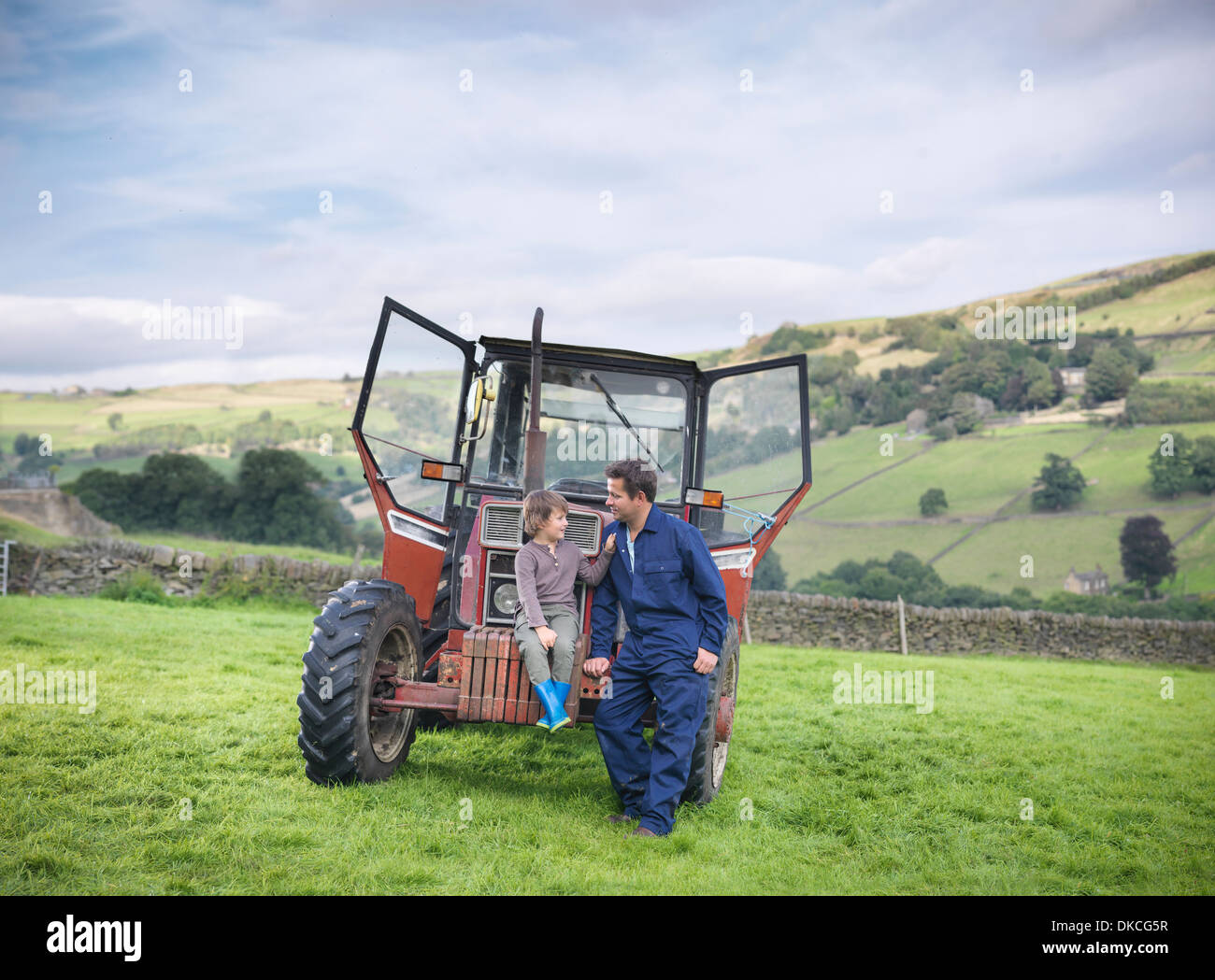Farmer and young son sitting on tractor in field Stock Photo