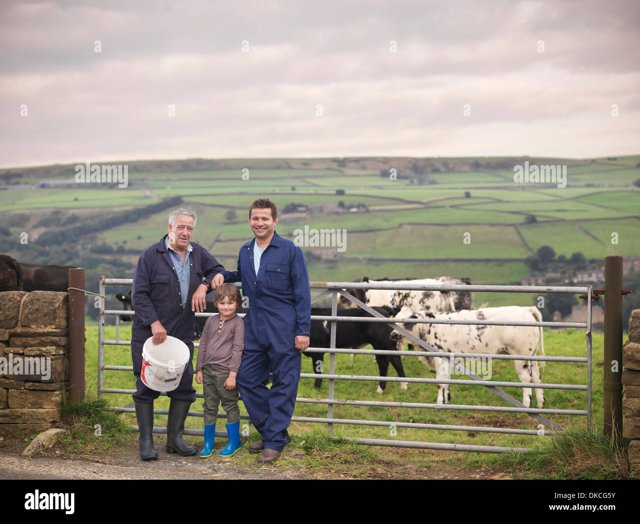 Mature farmer, adult son and grandson standing together at gate to cow field, portrait Stock Photo