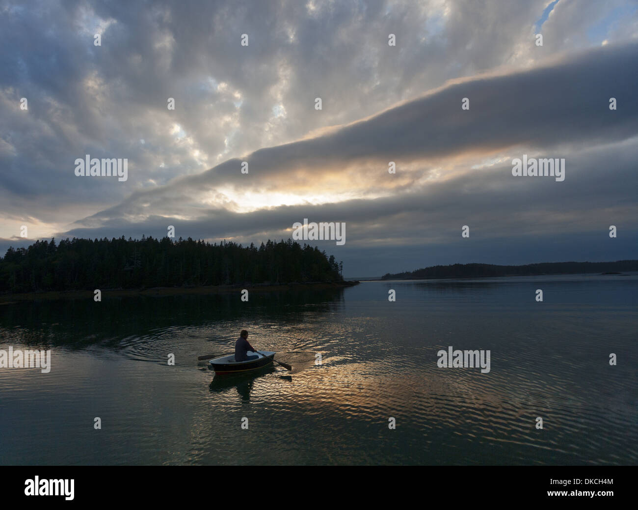 A man rows a dinghy at sunset under an interesting sky in Maine in Bunker's Cove, Roque Island, Maine, USA Stock Photo