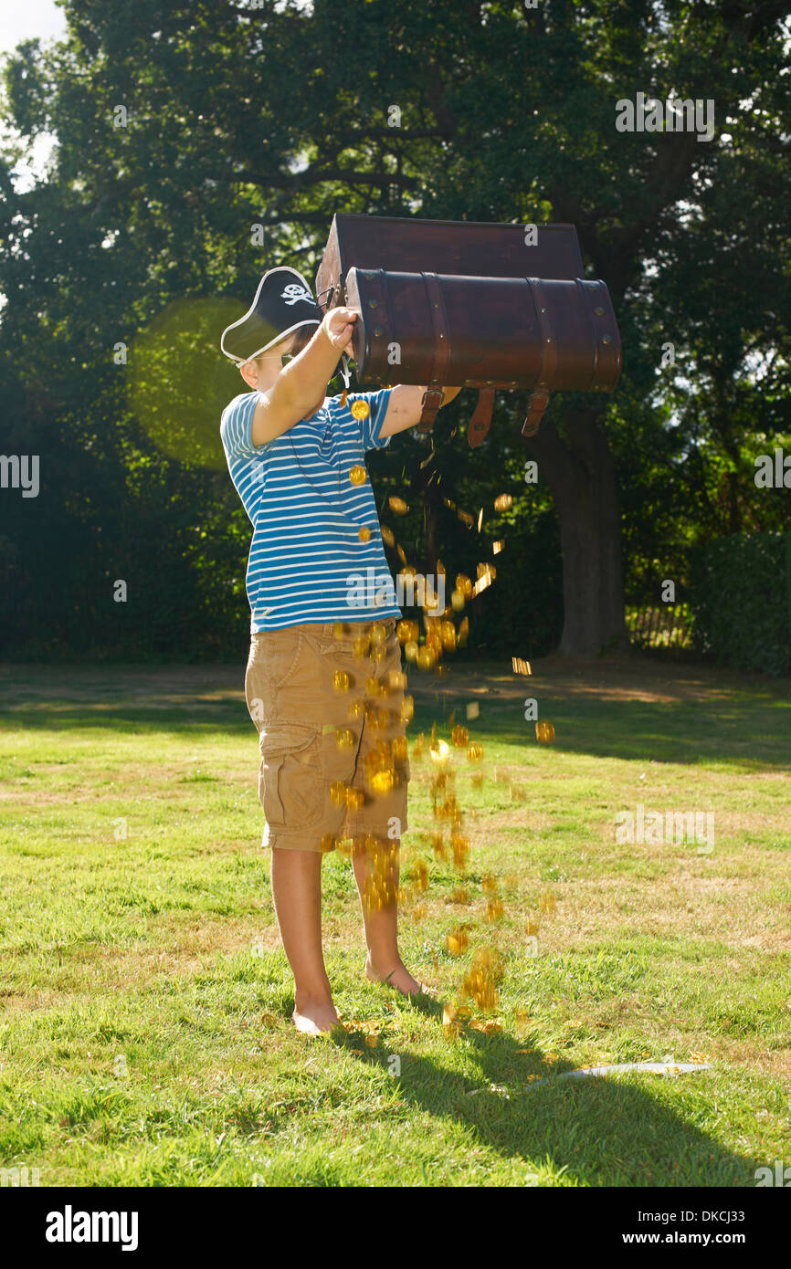 Boy dressed as pirate emptying gold from treasure chest in garden Stock Photo