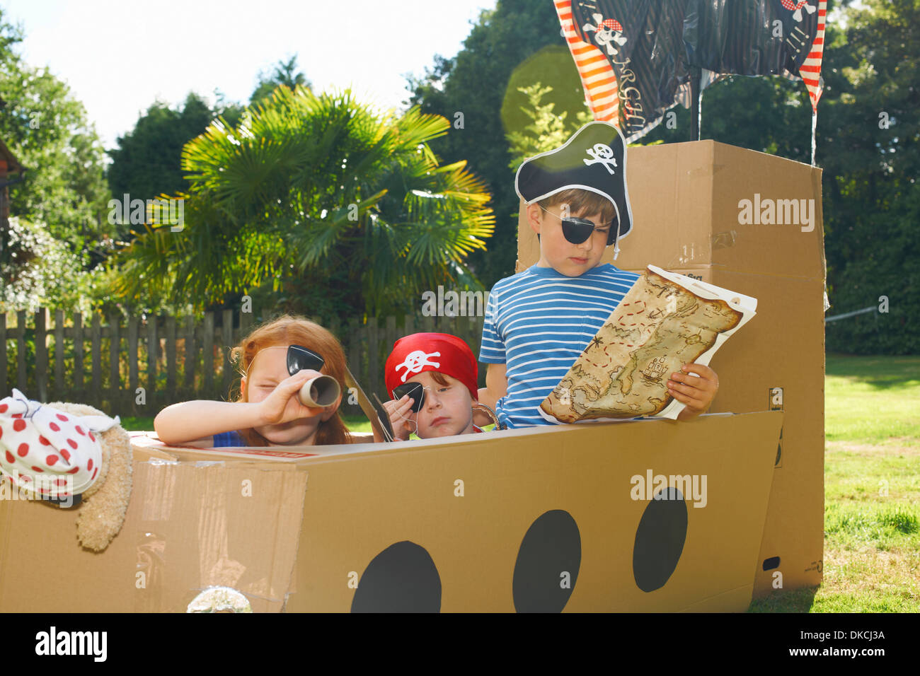 Two brothers and sister playing with homemade pirate ship in garden Stock Photo