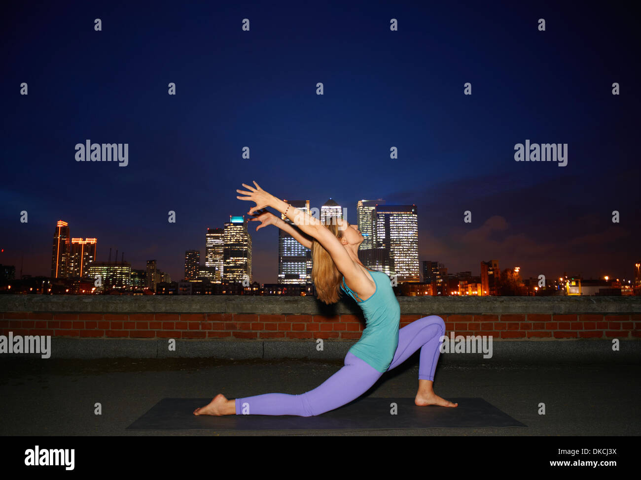 Mid adult woman doing yoga on city rooftop at night Stock Photo