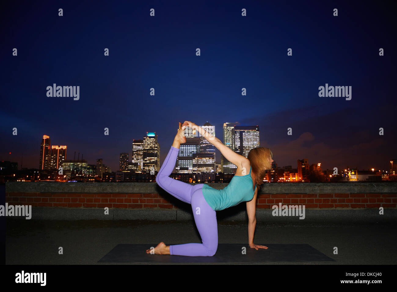 Mid adult woman practicing yoga on city rooftop at night Stock Photo