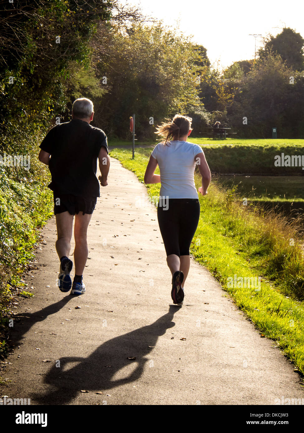 a male and female running in a public park beside a lake. Stock Photo