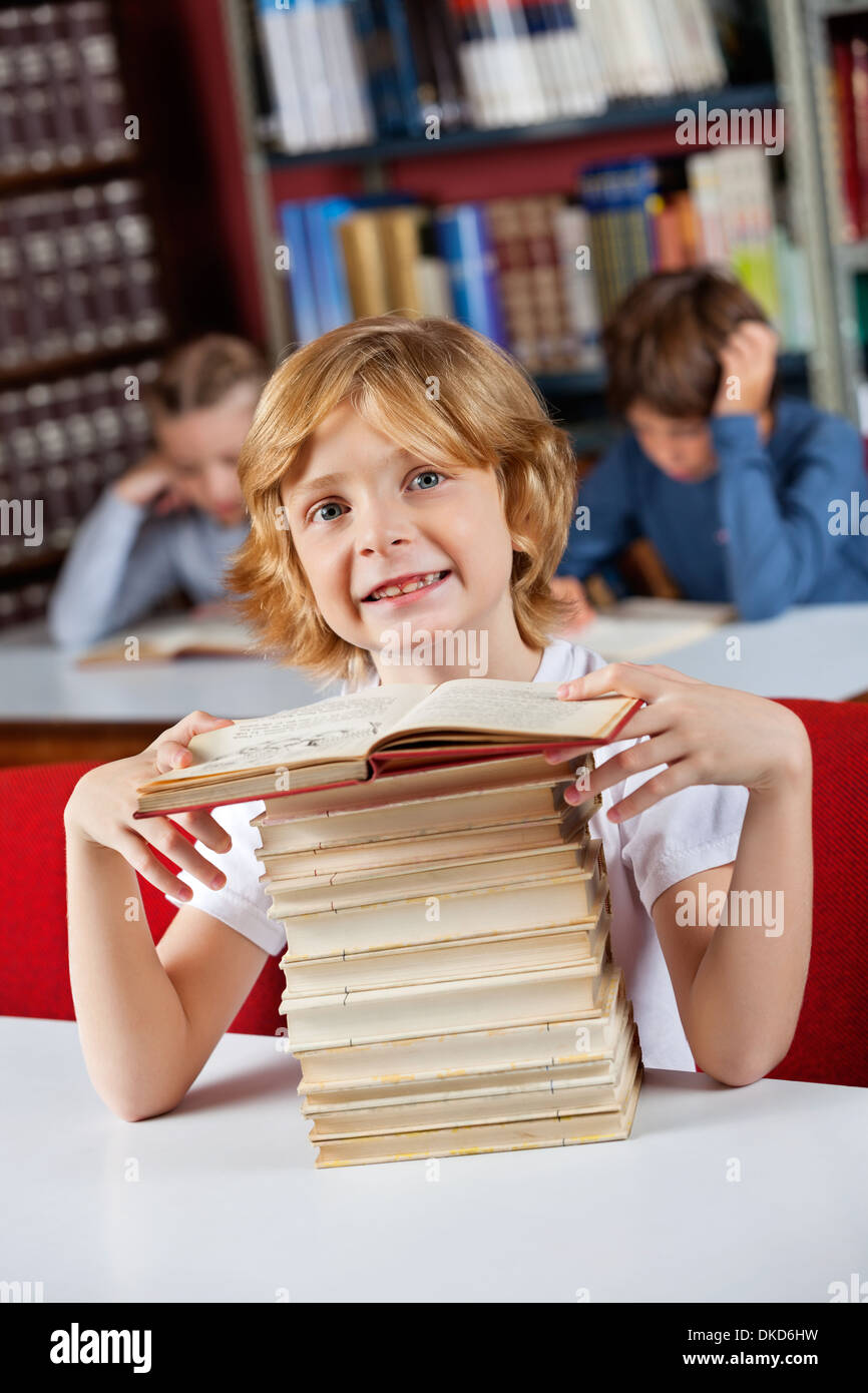 Schoolboy Smiling While Sitting With Stack Of Books In Library Stock ...