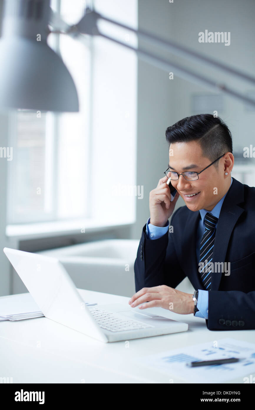 Young businessman in formalwear using laptop and calling in office Stock Photo