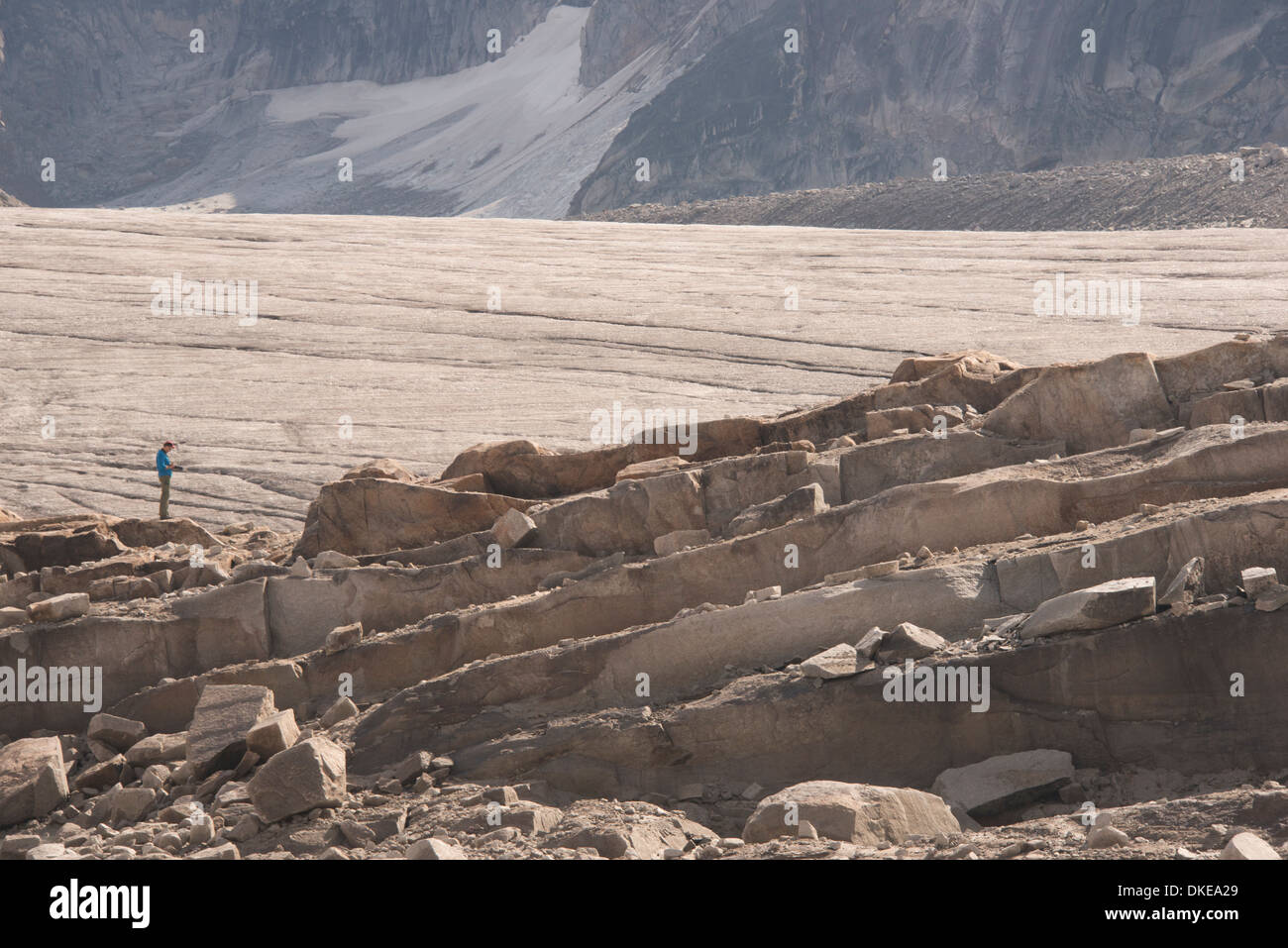 A lone figure contemplates the massive geological formations and ice at the foot of the Vowell Glacier in the mountains Stock Photo