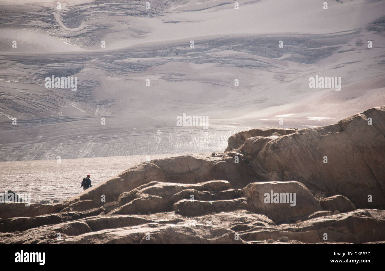 A lone figure navigates the boulders and ice of a glacier deep in the mountains. Stock Photo