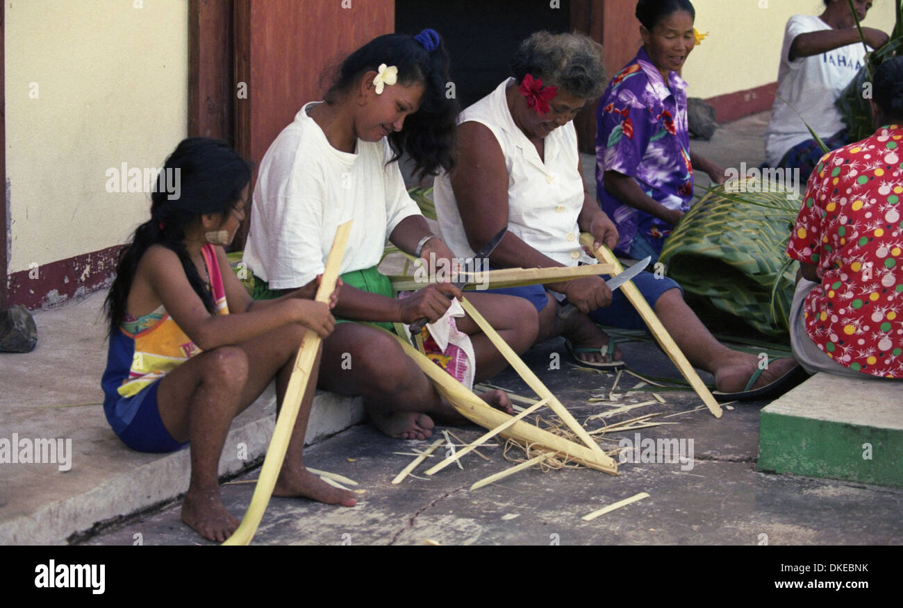 A group of Polynesian women weave baskets using materials from the