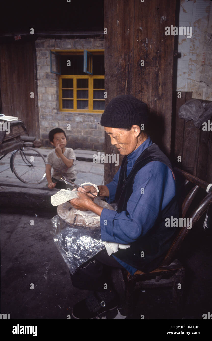 An old woman is making shoe indoor with a kid making funny face outdoor, photo taken in Hunan, China. Stock Photo