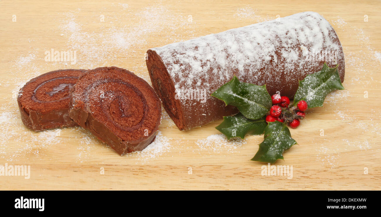 Christmas chocolate log on a wooden board dusted with icing sugar with holly, panoramic format Stock Photo