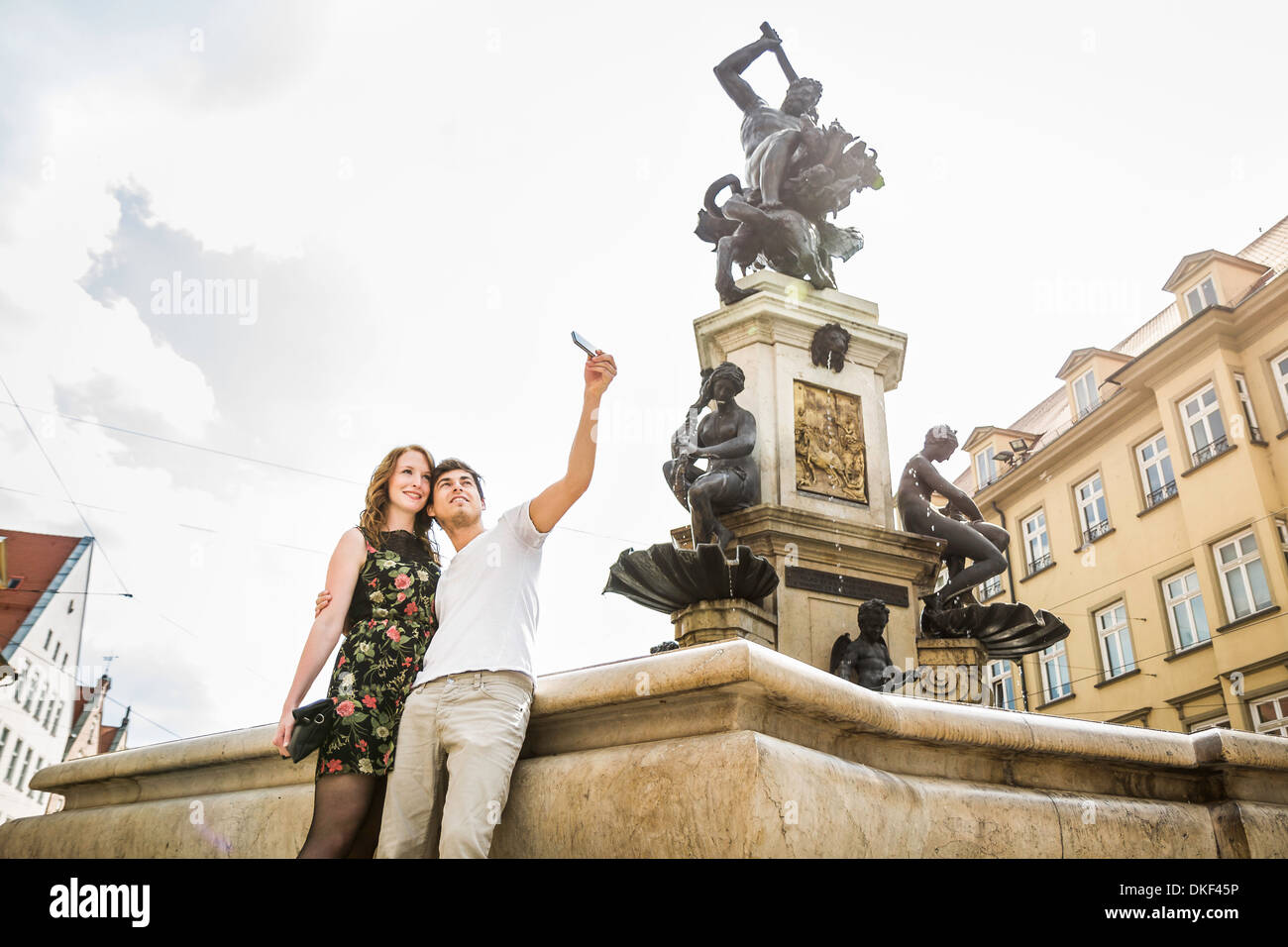Young couple taking self portrait photograph beside statue in Augsburg, Bavaria, Germany Stock Photo