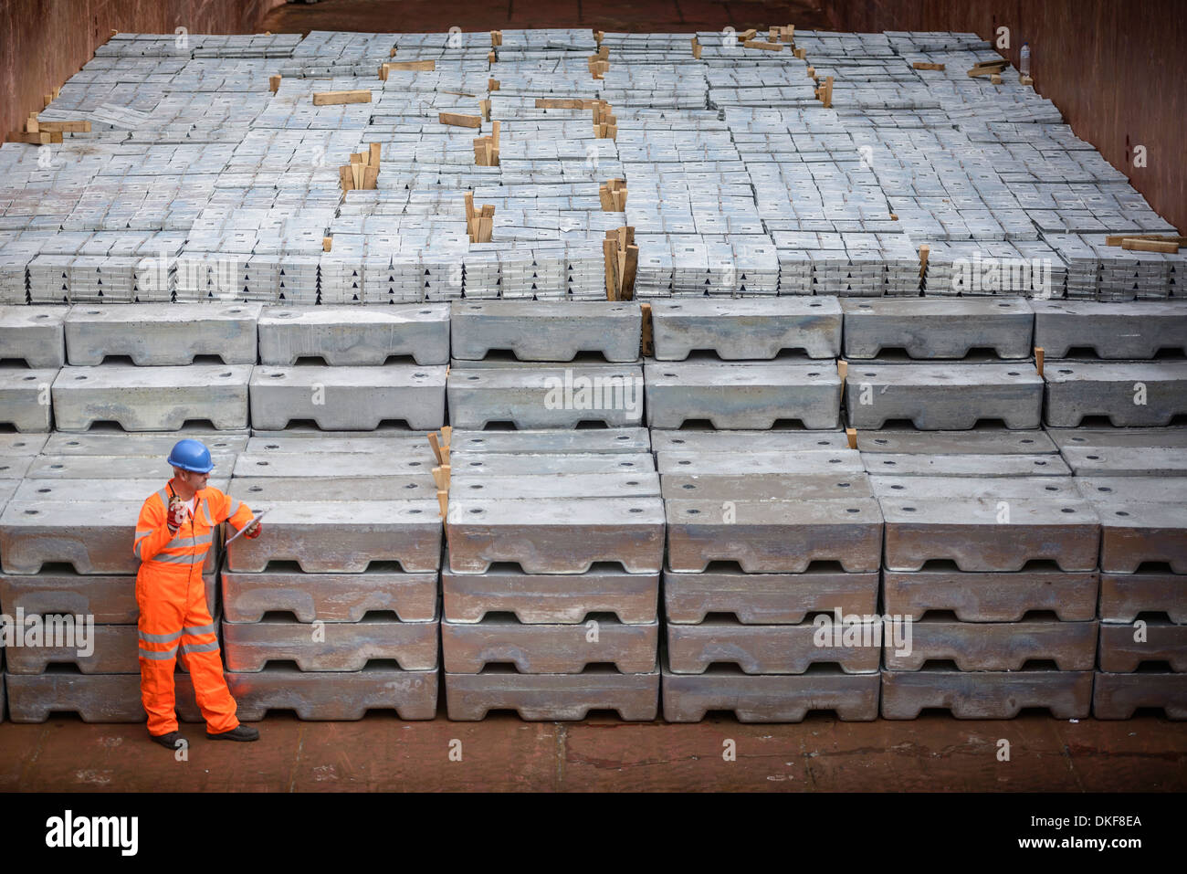 Worker standing next to metal ingots in ship's hold Stock Photo