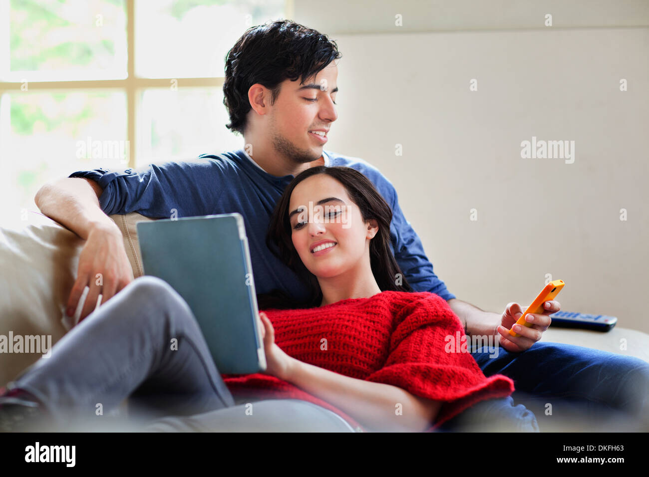 Young couple with digital tablet and mobile on living room sofa Stock Photo