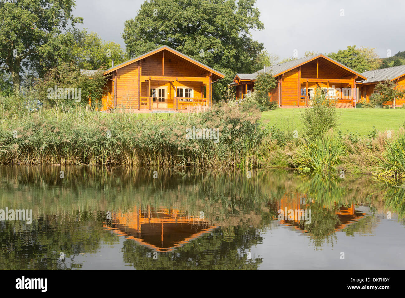 Holiday wooden Scandanavian lodges reflected in the waters of a small lake at Woodside Country Park, Ledbury, Herefordshire Stock Photo