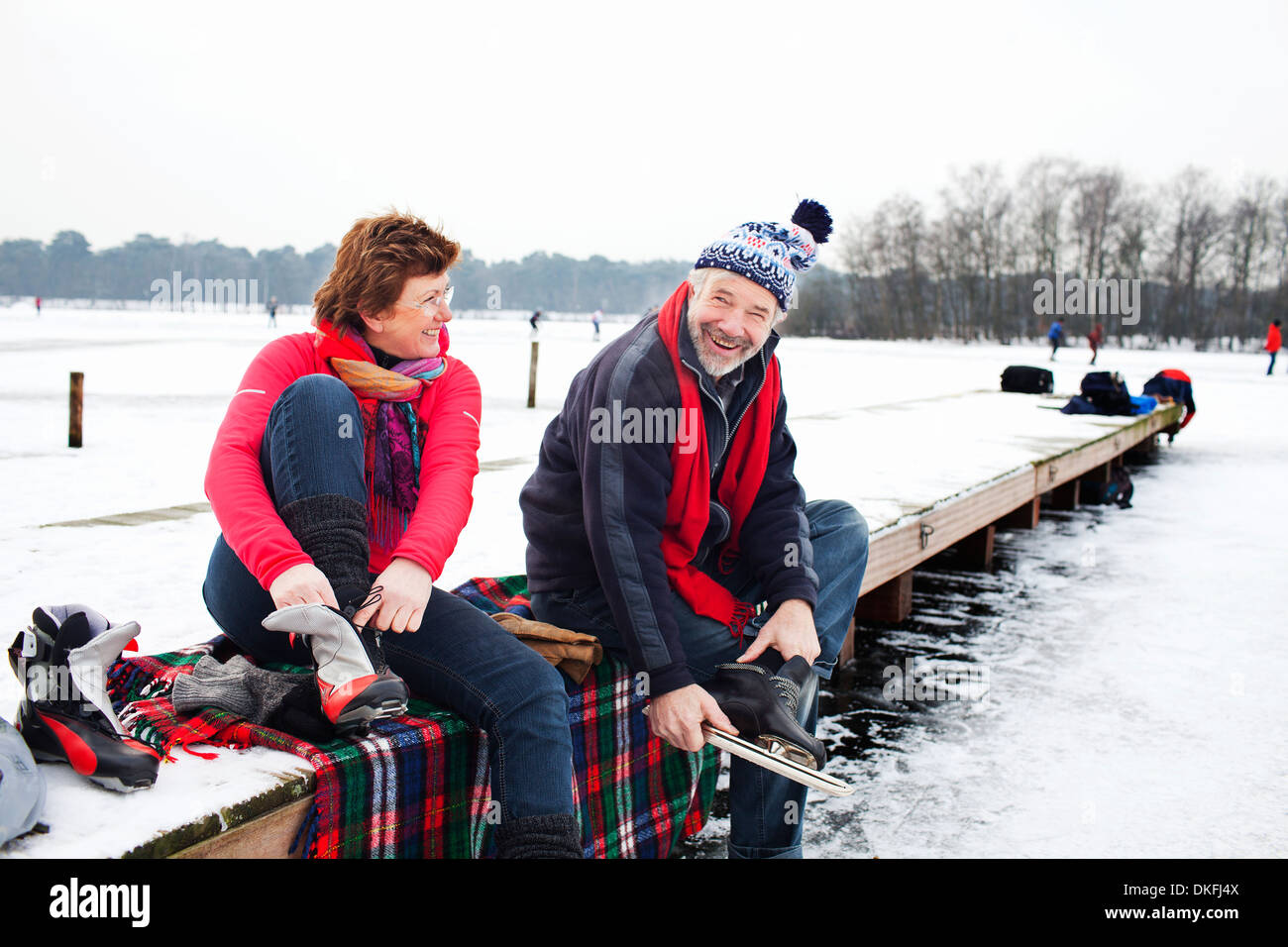 Couple sitting on pier putting on ice skates Stock Photo