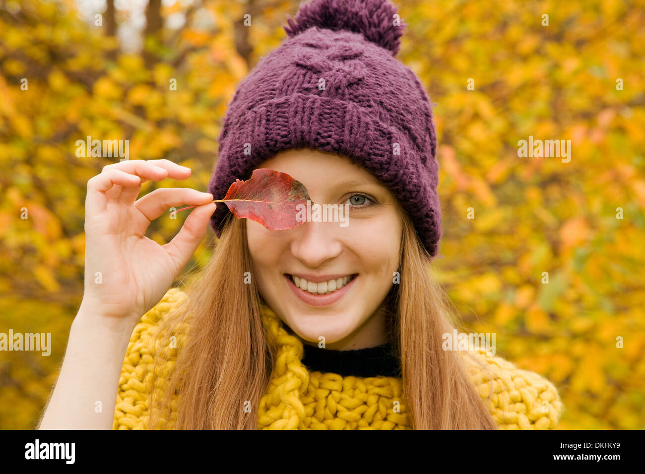 Close up of young woman in park holding autumn leaf over her eye Stock Photo