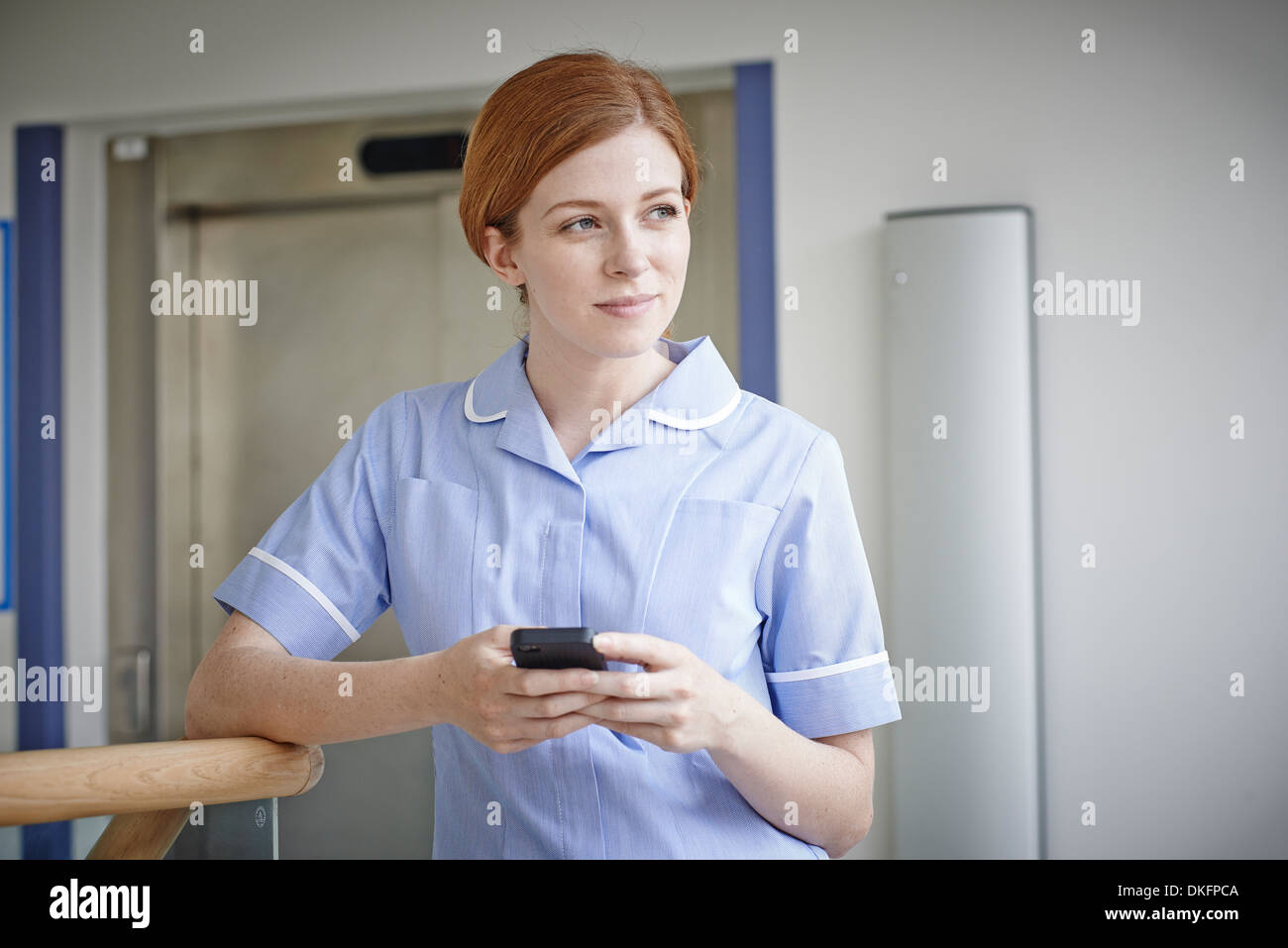 Female nurse with mobile phone outside hospital lift Stock Photo