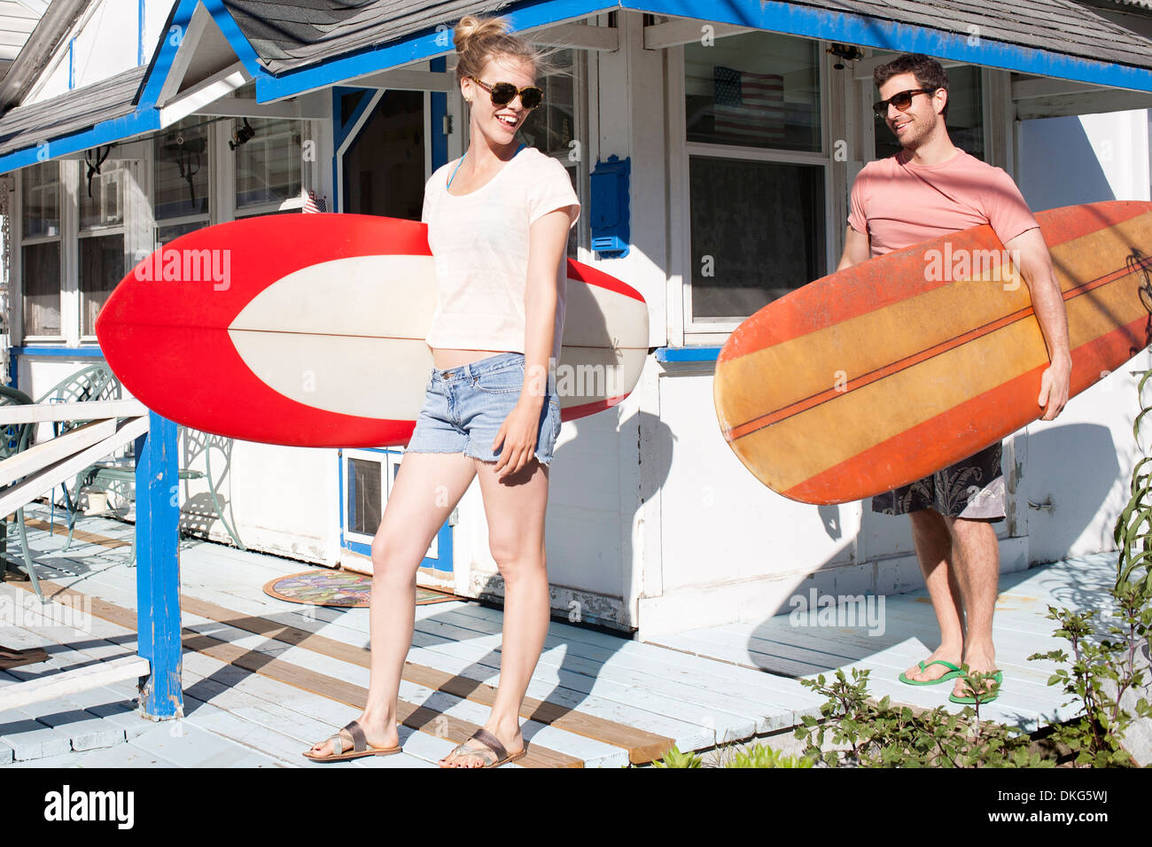 Couple on patio carrying surfboards, Breezy Point, Queens, New York, USA Stock Photo
