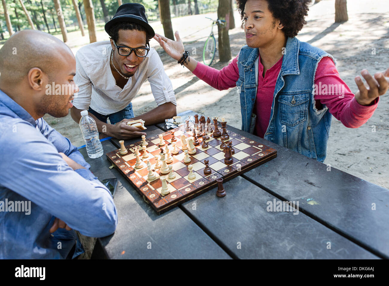 Three young men playing chess in park Stock Photo